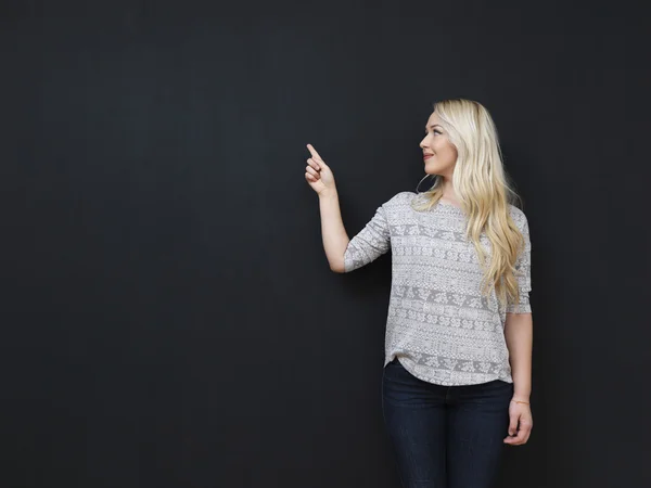 Mooie blonde op het schoolbord achtergrond wijzen met vinger — Stockfoto