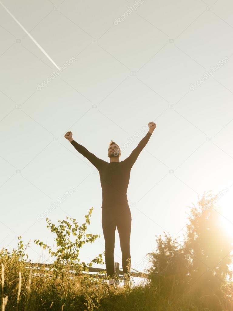 Successful man raising arms after cross track running on summer