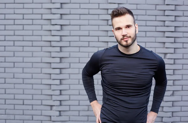 Corredor masculino sonriente en camiseta de pie contra la pared de cemento backgound — Foto de Stock