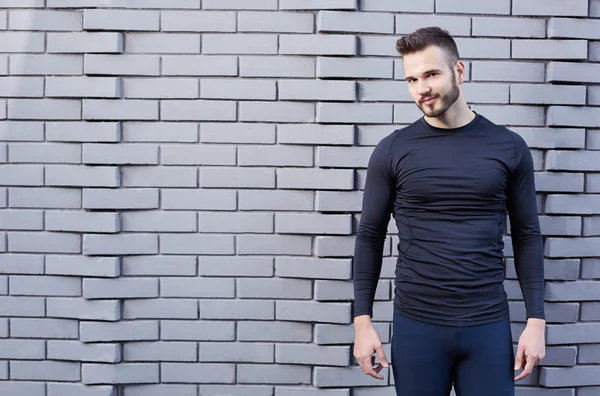 Sorrindo corredor masculino em t-shirt de pé contra backgound parede de cimento — Fotografia de Stock
