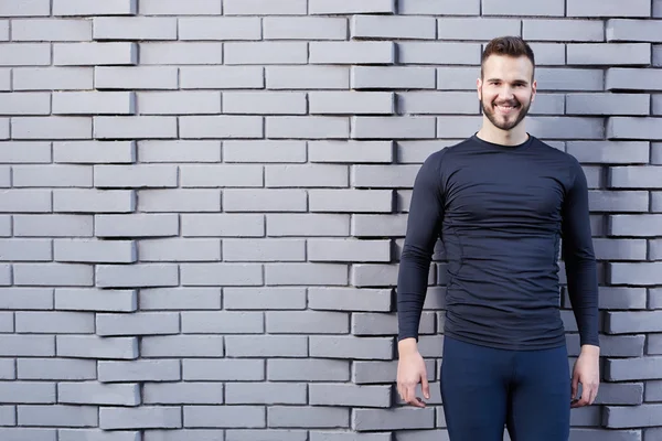 Corredor masculino sonriente en camiseta de pie contra la pared de cemento backgound — Foto de Stock
