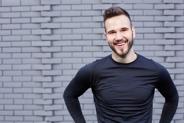 Smiling male runner in  t-shirt  standing against cement wall ba