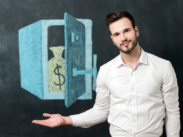 Joven con barba delante de la caja fuerte sonriendo y mostrando dinero — Foto de Stock