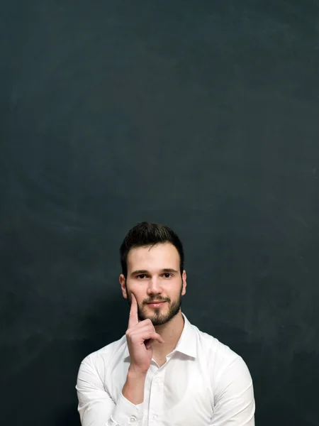 Portrait of a serious young man standing against chalkboard — Stock Photo, Image