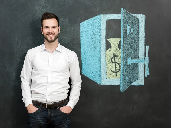 Joven con barba delante de la caja fuerte sonriendo y mostrando dinero — Foto de Stock