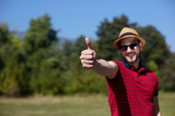 Молодой случайный человек, показывающий большие пальцы и улыбающийся в парке — стоковое фото