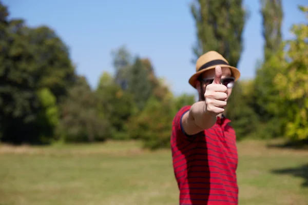 Casual ung visar tummen och ler i parken — Stockfoto