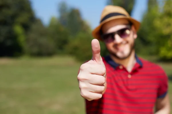 カジュアルな若者親指を示し、公園で笑顔 — ストック写真