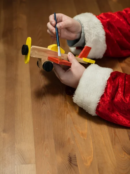 Julenissen sitter på verkstedet og maler et lekefly. Hor – stockfoto