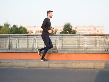 Sağlıklı görünümlü genç adam çapraz köprü sabah güneş altında koşu
