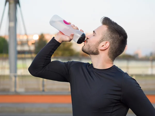 Jonge knappe loper met water fles zittend op een brug — Stockfoto