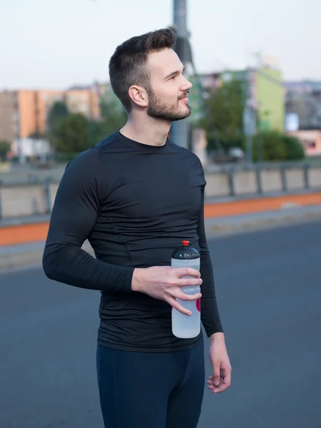 Young handsome runner with water bottle sitting on a bridge — Stock Photo, Image