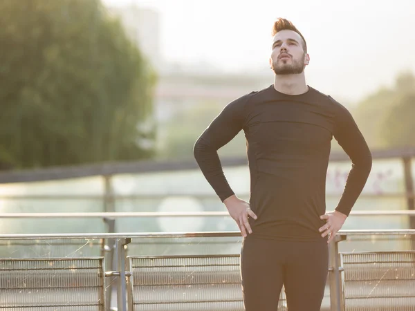 Joven hombre guapo corriendo a lo largo del terraplén cerca del río u — Foto de Stock