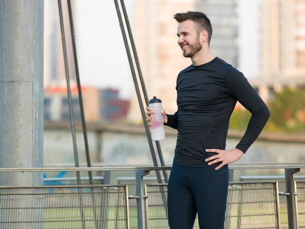 Joven hombre guapo corriendo a lo largo del terraplén cerca del río u — Foto de Stock