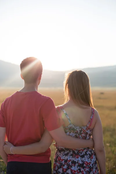 Jovem casal desfrutando o pôr do sol no prado — Fotografia de Stock