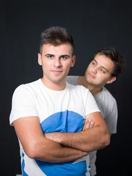 Man seriously posing while his friend is behind him fooling with him — Stock Photo, Image