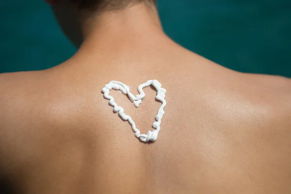 Hombre con loción bronceadora en la playa en forma de símbolos de amor — Foto de Stock