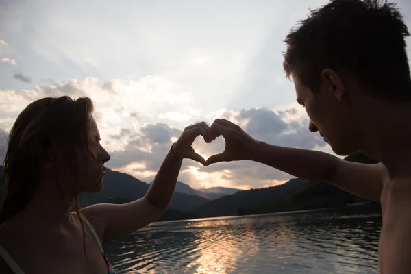 Pareja joven haciendo forma de corazón con los brazos en la playa contra Golde — Foto de Stock