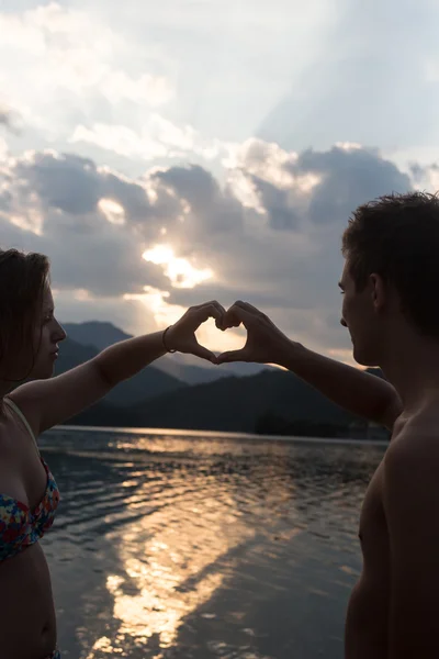 Jeune couple faisant forme de coeur avec les bras sur la plage contre l'or — Photo