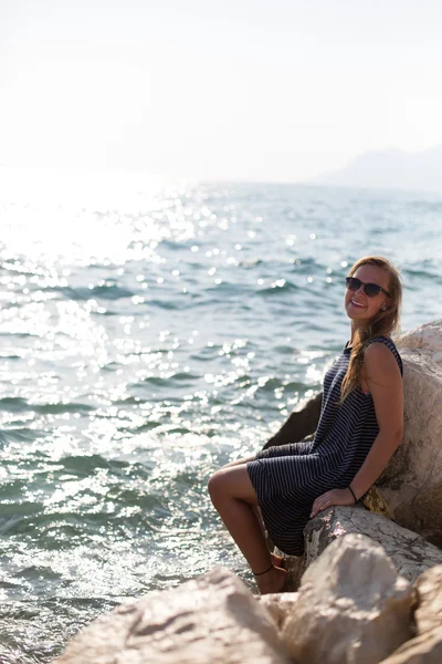 Hermosa mujer sentada en una piedra y salpicando en el mar —  Fotos de Stock