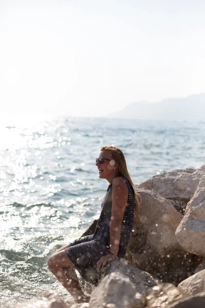 Beautiful woman sitting on a stone and splashing in the sea — Stock Photo, Image