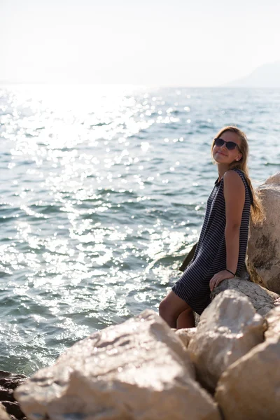 Gyönyörű nő ül egy kövön és fröccsen a tenger — Stock Fotó