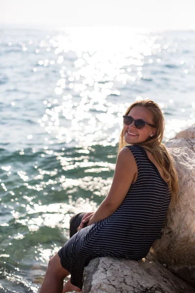Красивая женщина сидит на камне и брызгает в море — стоковое фото