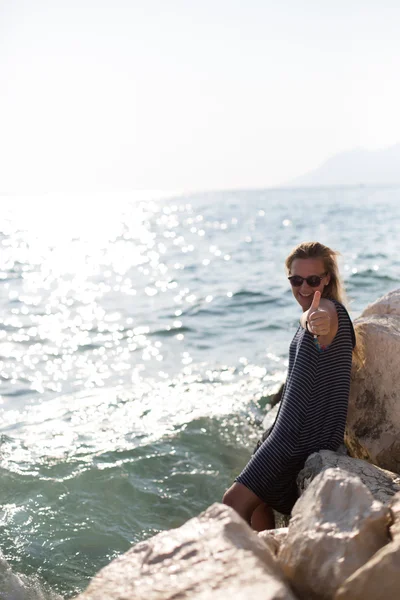 Hermosa mujer sentada en una piedra y salpicando en el mar — Foto de Stock