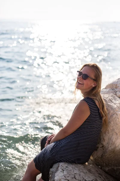 Bir taş üzerinde oturan ve denizde sıçramasına güzel kadın — Stok fotoğraf