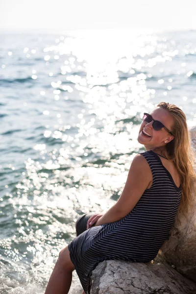 Hermosa mujer sentada en una piedra y salpicando en el mar —  Fotos de Stock