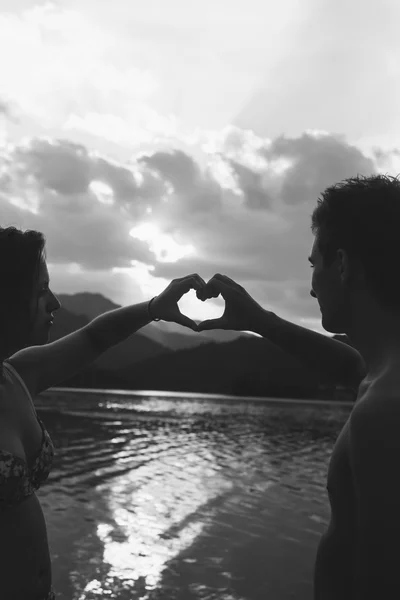 Jovem casal fazendo forma de coração com braços na praia contra golde — Fotografia de Stock