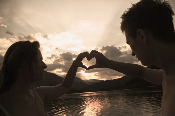 Young couple making heart shape with arms on beach against golde — Stock Photo, Image