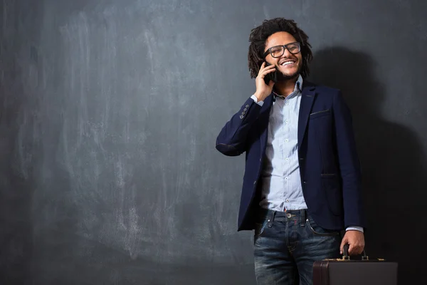 Foto di giovane afro con valigia sulla lavagna usando phon — Foto Stock