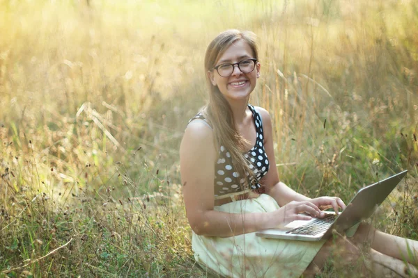 Happy woman working with a laptop in a green field with yellow f — Stock Photo, Image