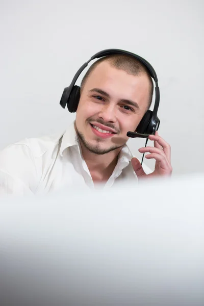 Sorrindo jovem casual com fone de ouvido usando computador — Fotografia de Stock