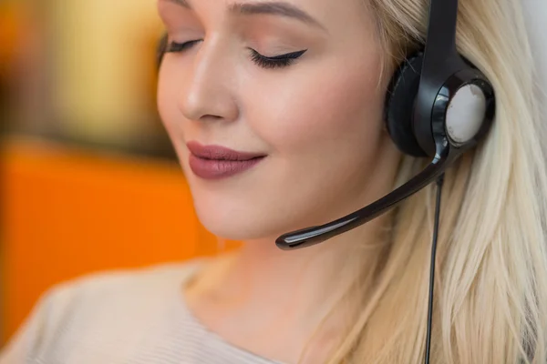 Κοντινό πλάνο μια ξανθιά χαμογελαστό γυναίκα φοράει ακουστικά στο γραφείο της — Φωτογραφία Αρχείου