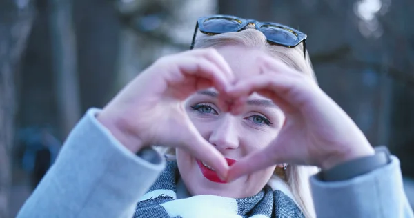 Mooie Kaukasische blonde vrouw toont hart teken met vinger — Stockfoto
