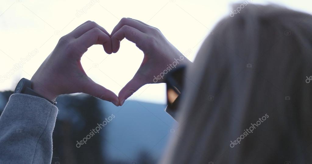 Beautiful caucasian blonde woman  showing heart sign with finger