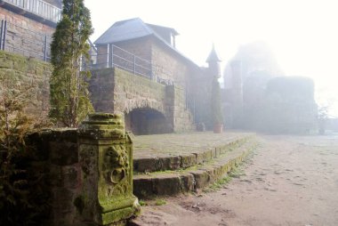 Landstuhl, Almanya 'da sisli, sisli bir sabahta Burg Nanstein (Nanstein Kalesi). 1162 civarında inşa edilmiş. Yosun koyları oyulmuş aslanlı kale girişi.. 