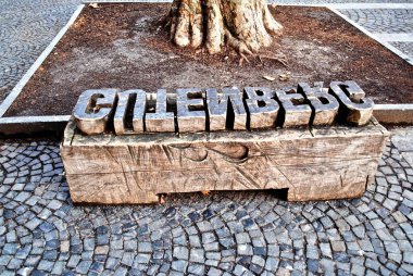 Hareketli ahşap baskı bloğu gibi görünmesi için oyulmuş bir bank. Hareket edebilen tip mucidi Johannes Gutenberg 'in adını verdiği Gutenberg Müzesi' nin önünde duruyor.. 