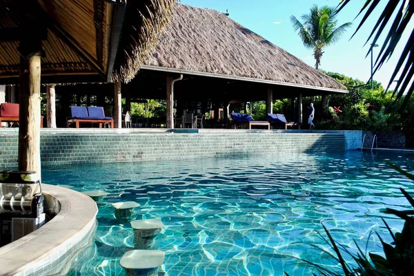 A swim-up pool bar in a turquoise swimming pool. Traditional Fiji bure thatched style roof. At the Outrigger Fiji Beach Resort.