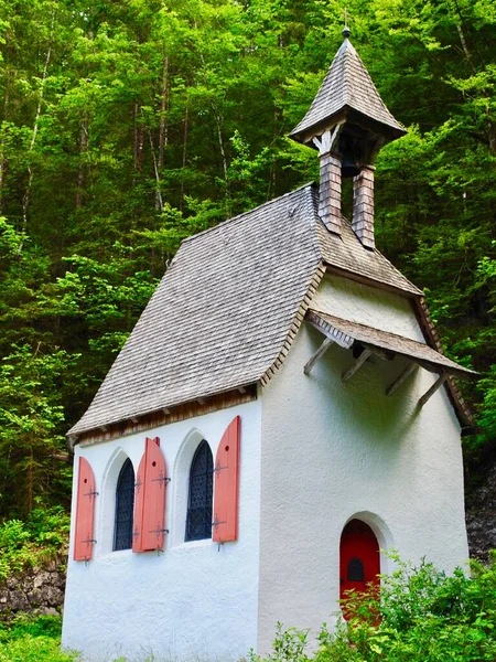 St. Johann und Paul Kapelle (St John and Paul Chapel) in the Berchtesgaden National Park, Bavaria, Germany. Very small, white Bavarian chapel with red shutters and door, steep roof and bell tower.