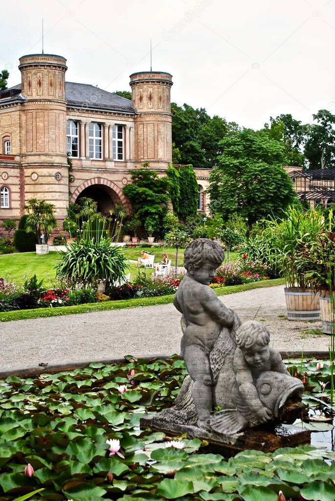 KARLSRUHE, GERMANY: Botanical gardens (Botanischer Garten Karlsruhe) with old gate building, palace grounds, lily pond, and statue of two cherubs playing with a carp in the water.