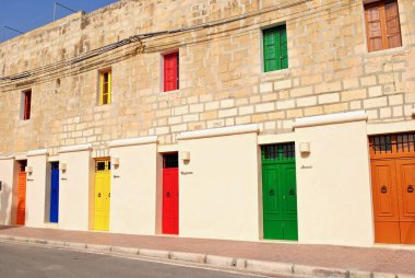 Marsaxlokk, Malta: Balıkçı köyündeki çok renkli kapı ve panjurlar Turuncu, sarı, kırmızı, yeşil ve kahverengi kapılar yol kenarındaki parlak kireçtaşı sıva ve tuğla bina. 