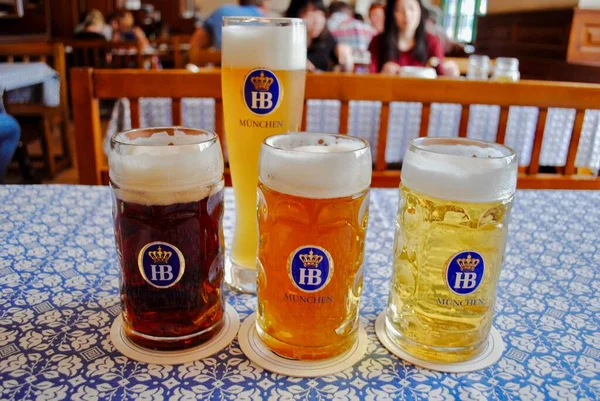 Münih, Almanya: Hofbrauhaus (Hofbruhaus) birası - Dunkel (koyu), Helles (lager), Radler (limonata ile karıştırılmış), Weibier (buğday) mavi ve beyaz masa örtüsü üzerine HB bira bardakları (ma olarak adlandırılır). 