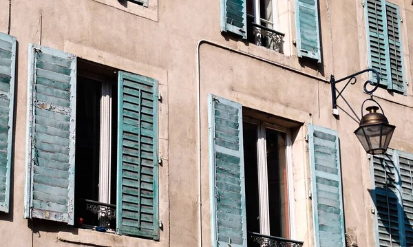 Teal shutters on rows of windows on a tan building in Nancy, France. Wooden, antique, rustic, typical Lorraine building with pastel teal, sea foam, or aqua window shutters and a traditional lantern.