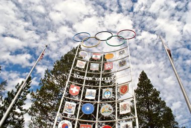 Olimpiyat Vadisi, Kaliforniya: Olimpiyat ateşi, uluslararası bayraklar ve Olimpiyat Vadisi Kayak Tesisi tabelasında Olimpiyat yüzükleri. 1960 Kış Olimpiyatlarının ev sahibi..