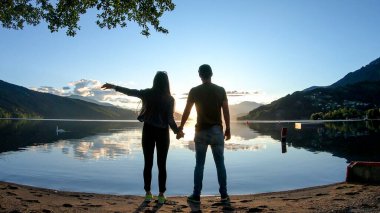 Millstaetter Gölü kıyısında gün batımında el ele tutuşan bir çift. Güneş yüksek Alpler 'in arkasında batar. Gölün sakin yüzeyi turuncu gökyüzünü yansıtır. Onlar eğleniyorlar. Gün sonu