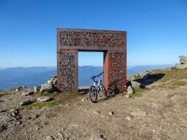 Avusturya Alplerinde Granattor 'un altına park edilmiş bir dağ bisikleti. Metal kapı granit taşlarla dolu. Arkadaki yüksek dağ zincirleri. Etrafta bir sürü kayıp taş var. Yavaş yol. Açık hava aktiviteleri