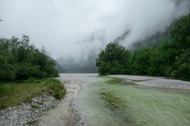 Avusturya 'daki Leopoldsteiner Gölü manzaralı. Göl kalın sisle kaplı yüksek Alplerle çevrilidir. Yağmurlu bir hava. Sığ su kristal berraklığında, kaynak suyunun sakin bir yüzeyi var. Huzur
